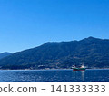 A cargo ship floating on a calm sea and a mountain range with wind turbines. 141333333