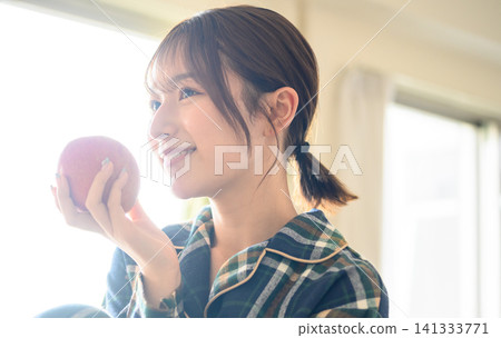 A smiling woman holding an apple in her room A smiling woman holding an apple in her room 141333771