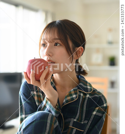 一位身穿睡衣的女士正在享受輕鬆的早晨,一邊吃蘋果。 一位身穿睡衣的女士正在享受輕鬆的早晨,一邊吃蘋果。 141333773