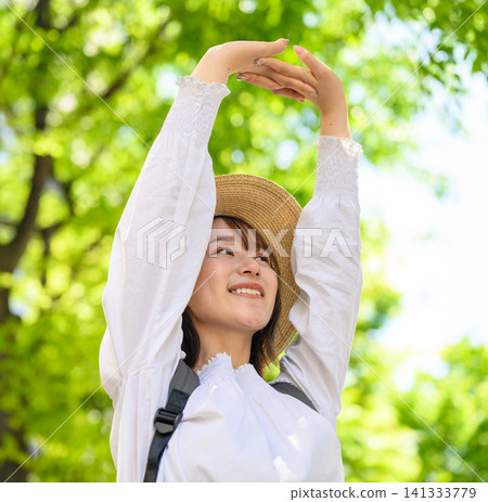 A woman wearing a straw hat stretches amidst the fresh greenery. A woman wearing a straw hat stretches amidst the fresh greenery. 141333779