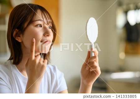 一位女士正用手鏡檢查自己的皮膚。 141333805