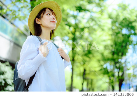 一位戴著草帽的女子漫步在綠樹成蔭的街道上。 一位戴著草帽的女子漫步在綠樹成蔭的街道上。 141333806