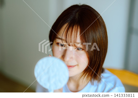 A woman checking her skin in the mirror 141333811
