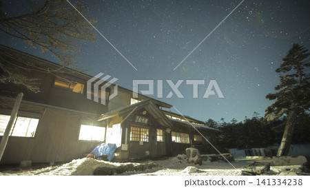 Winter snow-covered mountains and a mountain hut at night, with a sky full of stars. Winter snow-covered mountains and a mountain hut at night, with a sky full of stars. 141334238