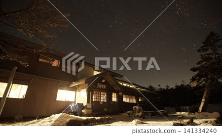Winter snow-covered mountains and a mountain hut at night, a beautiful starry sky. Winter snow-covered mountains and a mountain hut at night, a beautiful starry sky. 141334240