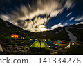 A mountain campsite illuminated by moonlight and flowing clouds. 141334278