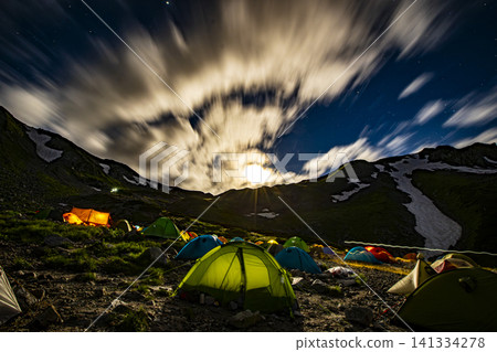 A mountain campsite illuminated by moonlight and flowing clouds. 141334278