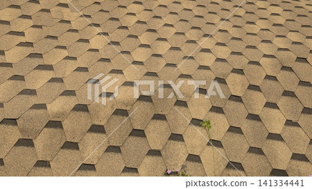 A horizontal high angle perspective captures a repeating geometric pattern of hexagonal asphalt roof shingles. The textured surface displays brown tan tones with dark shadow lines, creating a A horizontal high angle perspective captures a repeating geometric pattern of hexagonal asphalt roof shingles. The textured surface displays brown tan tones with dark shadow lines, creating a 141334441