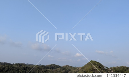 A horizontal wide angle perspective captures lush green forest hills stretching across the horizon under a vast blue sky. Scattered white clouds drift gently above the rolling tropical mountain A horizontal wide angle perspective captures lush green forest hills stretching across the horizon under a vast blue sky. Scattered white clouds drift gently above the rolling tropical mountain 141334447