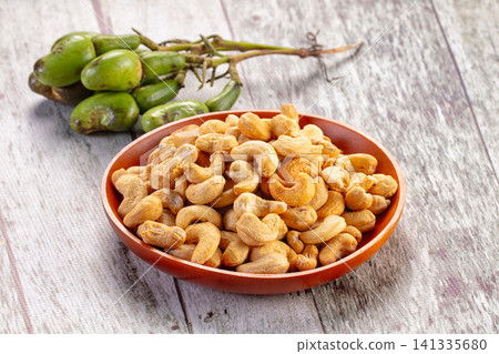Roasted cashew nuts in wooden bowl with raw green cashew fruit on rustic wood 141335680