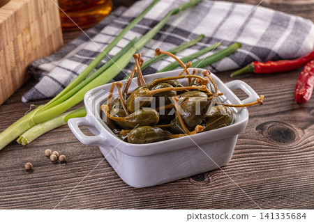 Pickled caper berries in white ceramic bowl with green onions and red chili on rustic wood Pickled caper berries in white ceramic bowl with green onions and red chili on rustic wood 141335684
