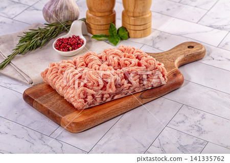Raw ground chicken on wooden cutting board with rosemary garlic and peppercorns Raw ground chicken on wooden cutting board with rosemary garlic and peppercorns 141335762