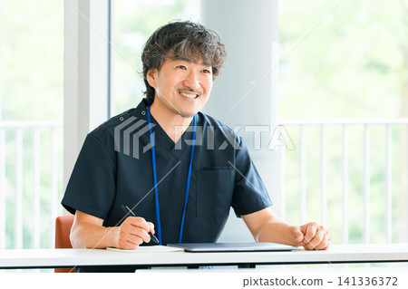 A male doctor, surgeon, or physician in scrubs sitting at a table. A male doctor, surgeon, or physician in scrubs sitting at a table. 141336372