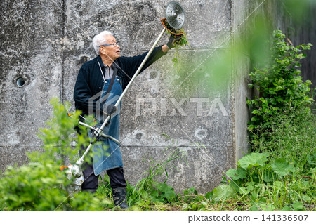 Elderly man mowing with a mower in early summer Elderly man mowing with a mower in early summer 141336507