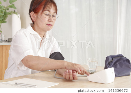 Senior woman measures and records her blood pressure at home 141336672