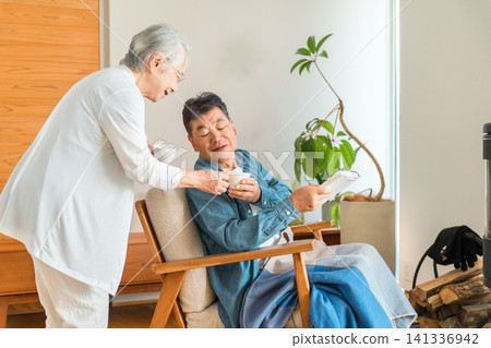 A senior couple relaxing in the living room while drinking coffee. A senior couple relaxing in the living room while drinking coffee. 141336942