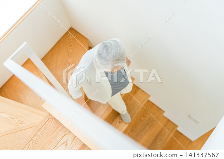 A senior woman with gray hair descends the stairs of her home. A senior woman with gray hair descends the stairs of her home. 141337567