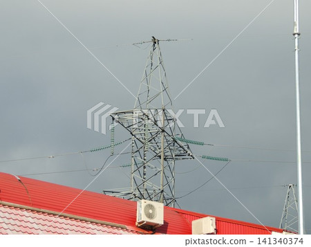 A high-voltage power transmission tower with wires and insulators rises above the building's metal roof. External air conditioning units are mounted on the roof, a feature of the industrial landscape. 141340374