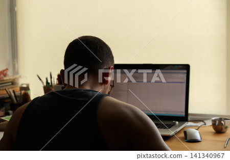 Back view of a man working on a laptop at his desk in a home office, concept of remote work and digital productivity. Back view of a professional man working on a laptop at his home office desk Back view of a man working on a laptop at his desk in a home office, concept of remote work and digital productivity. Back view of a professional man working on a laptop at his home office desk 141340967