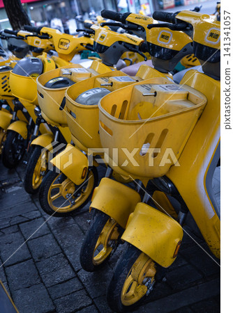 A fleet of modern, bright yellow shared e-bikes equipped with front baskets parked on a street. 141341057