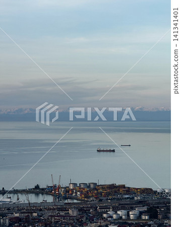 Wide view of Batumi cargo port and Black Sea coast with docked ships, storage tanks, and snowy Caucasus Mountains Wide view of Batumi cargo port and Black Sea coast with docked ships, storage tanks, and snowy Caucasus Mountains 141341401