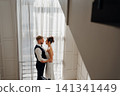 Portrait of a beautiful groom and a bride by the window 141341449