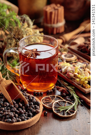 Rustic herbal tea with anise, dried citrus, juniper berries and aromatic spices in a glass mug. Rustic herbal tea with anise, dried citrus, juniper berries and aromatic spices in a glass mug. 141341531