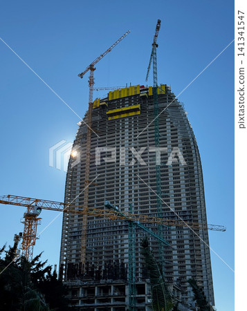 High-rise building under construction with cranes against clear blue sky. High-rise building under construction with cranes against clear blue sky. 141341547