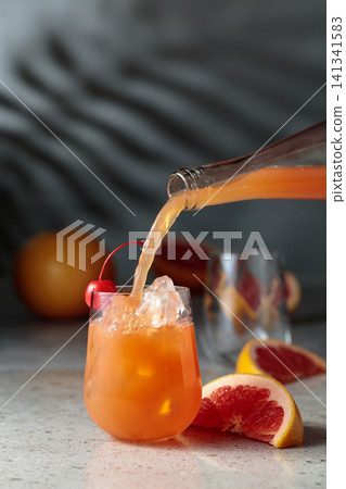 Grapefruit juice is poured into a glass with ice. Grapefruit juice is poured into a glass with ice. 141341583