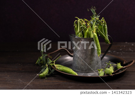 Fresh green pea pods standing in vintage metal pitcher Fresh green pea pods standing in vintage metal pitcher 141342323