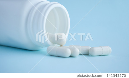 medicine pills capsule spilling out of bottle on blue background medicine pills capsule spilling out of bottle on blue background 141343270