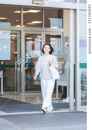 A smiling woman walks out of the supermarket entrance with an eco-bag in her hand. 141343845