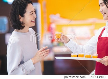 A female customer smiles as she receives a free sample of juice at the front of the supermarket. A female customer smiles as she receives a free sample of juice at the front of the supermarket. 141343900