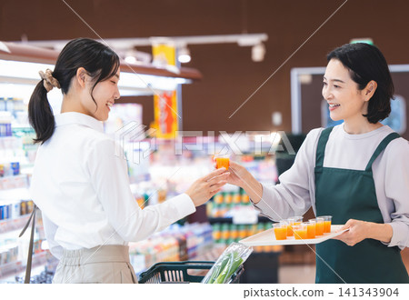 A female store clerk at a supermarket, smiling and offering samples to customers. 141343904