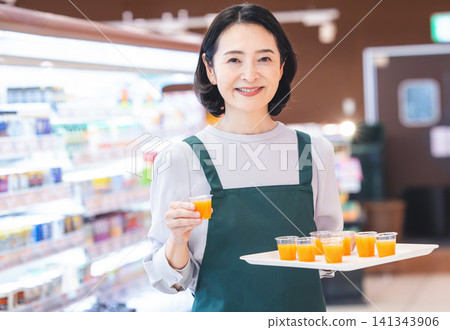 超市入口處的女售貨員微笑地提供試吃樣品。 超市入口處的女售貨員微笑地提供試吃樣品。 141343906