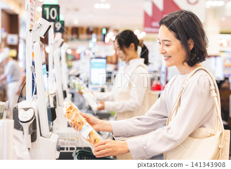 A smiling female customer scans the barcodes of her items at a self-checkout counter. A smiling female customer scans the barcodes of her items at a self-checkout counter. 141343908