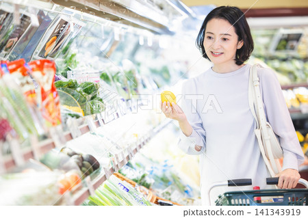 一位五十多歲、舉止優雅的女士在蔬菜區拿起一顆檸檬。 一位五十多歲、舉止優雅的女士在蔬菜區拿起一顆檸檬。 141343919