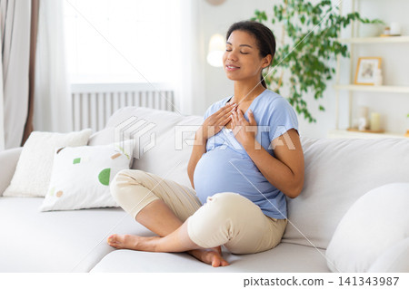 Black pregnant woman practicing calm breathing with eyes closed, hands on chest Black pregnant woman practicing calm breathing with eyes closed, hands on chest 141343987