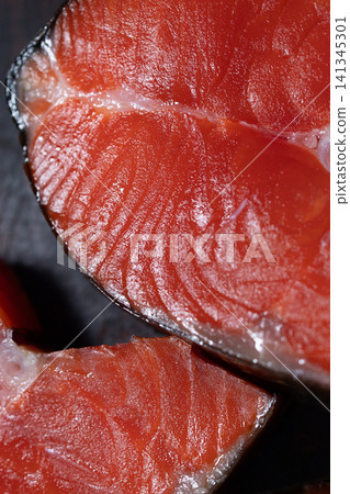 Smoked sockeye salmon steak with glossy red flesh, delicate muscle fibers, thin white connective tissue, rich cured surface, and dark background for dramatic food presentation Smoked sockeye salmon steak with glossy red flesh, delicate muscle fibers, thin white connective tissue, rich cured surface, and dark background for dramatic food presentation 141345301
