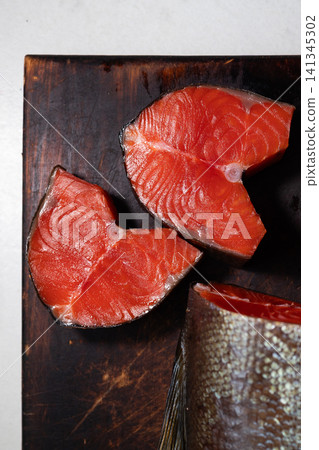 Closeup smoked sockeye salmon steaks arranged on dark wooden board, showing vivid red flesh, glossy oily sheen, rich texture, and partial tail for rustic food presentation Closeup smoked sockeye salmon steaks arranged on dark wooden board, showing vivid red flesh, glossy oily sheen, rich texture, and partial tail for rustic food presentation 141345302