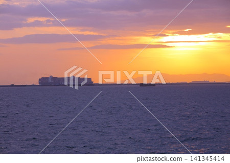 A container ship sailing off the coast of Kobe Port against the backdrop of the setting sun (viewed from the Naruo-hama Seaside Park fishing area). 141345414