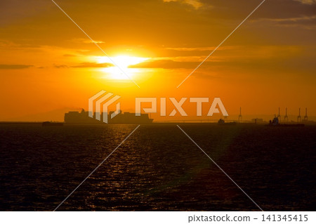 A large cargo ship sailing off the coast of Kobe Port, the Kobe Airport Bridge, and the setting sun (viewed from the Naruo-hama Seaside Park fishing area). A large cargo ship sailing off the coast of Kobe Port, the Kobe Airport Bridge, and the setting sun (viewed from the Naruo-hama Seaside Park fishing area). 141345415