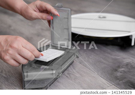 Close up of woman hands replacing or cleaning HEPA filter in robot vacuum dustbin Close up of woman hands replacing or cleaning HEPA filter in robot vacuum dustbin 141345529