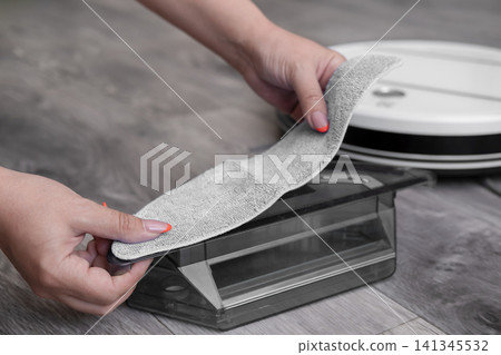 Close up of woman hands attaching microfiber mopping cloth to robot vacuum water tank 141345532