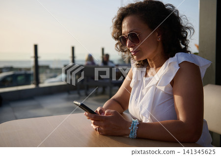 Woman using smartphone at outdoor cafe by the seaside during golden-hour Woman using smartphone at outdoor cafe by the seaside during golden-hour 141345625