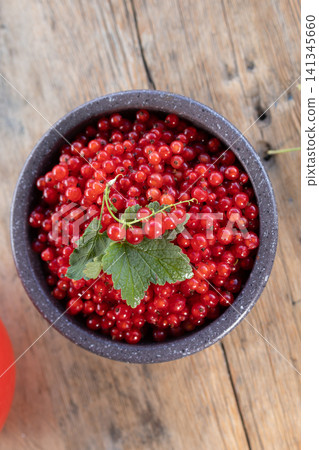 Ripe red currants in rustic ceramic bowl on weathered wooden table with green leaf, glossy clustered berries under soft natural light, fresh seasonal produce for healthy summer food concepts Ripe red currants in rustic ceramic bowl on weathered wooden table with green leaf, glossy clustered berries under soft natural light, fresh seasonal produce for healthy summer food concepts 141345660