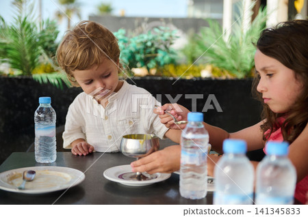 Young siblings sharing dessert at outdoor cafe as sister feeds little brother Young siblings sharing dessert at outdoor cafe as sister feeds little brother 141345833