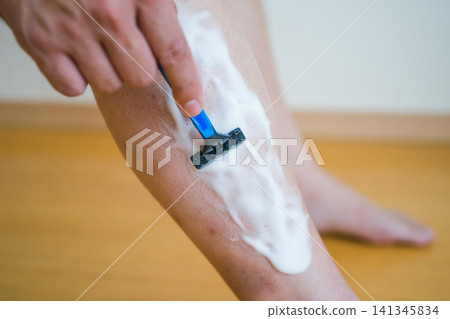 A scene of a man shaving the hair on his shins with a razor. A scene of a man shaving the hair on his shins with a razor. 141345834