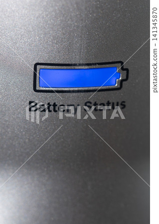 Blue battery indicator illuminated on textured metallic panel with partial status, closeup view showing recessed display, reflective grain, and subtle industrial detailing Blue battery indicator illuminated on textured metallic panel with partial status, closeup view showing recessed display, reflective grain, and subtle industrial detailing 141345870