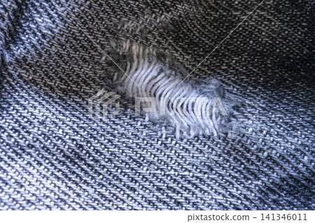 A close-up macro shot shows a rip in a dark woven fabric. A close-up macro shot shows a rip in a dark woven fabric. 141346011